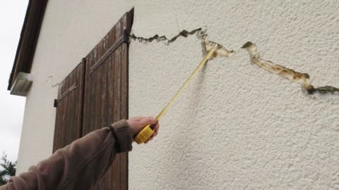 Mesure d'une fissure importante sur la façade de la maison lors de l'expertise avant achat